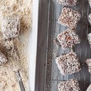 lamingtons<br /><br />Lamingtos are the stuff of an Aussie childhood. Making regular appearances at birthday parties, morning and afternoon teas and community fundraisers across the country, these simply delicious cakes are perfect for whipping up to celebrate Australia Day.<br /><br />For the cake<br />4 eggs<br />200g (1 cup) granulated sugar<br />1 teaspoon vanilla extract<br />200g (1 ⅓ cups) all-purpose (plain) flour<br />1 ½ teaspoons baking powder<br />110g butter, melted and cooled<br /><br />For the icing<br />75g unsalted butter<br />250ml (1 cup) milk<br />65g (1/2 cup) cocoa powder<br />435g (3 cups) icing sugar<br /><br />To assemble<br />Around 6 cups desiccated coconut<br /><br />Method for the sponge<br />Preheat the oven to 350˚F/180˚C/gas 4. Grease and flour a 20cm x 30cm pan, lining the base of the pan with parchment paper. Beat the eggs, sugar and vanilla in a large bowl with an hand mixer (medium-high speed) until pale and thick (around 3 minutes). Sift the flour and baking powder over the egg and sugar mixture and use a rubber spatula to gently combine the dry ingredients. Add the melted butter, about ⅓at a time, gently mixing with a rubber spatula until completely combined, then pour the mixture into the prepared pan.<br /><br />Bake for 25 minutes, or until a skewer inserted into the middle of the cake comes out clean. The cake should spring back when lightly touched in the centre. Turn cake onto a wire rack to cool.<br /><br />Cut cake into even, bit-sized pieces about 4-5cm.  You will probably end up discarding the edge pieces, as they won’t be completely square. At this stage you can refrigerate the cake for a few hours or leave the cake overnight in an airtight container, because a slightly less fresh cake will be easier to dip in the chocolate icing.<br /><br />When you are ready to dip the cakes, set up an area large enough to accommodate bowls for the cake pieces, the chocolate icing, the coconut and also a large tray topped with parchment paper and a cooling rack. You will need to work quickly to dip the cakes so having everything organised in advance will help.<br /><br />Method for the icing<br />Sift the icing sugar and the cocoa powder into two different bowls. In a large saucepan, melt the butter, then mix in the milk. Next, using a whisk to stir, start to add the cocoa powder. Once the cocoa powder is completely dissolved, add the icing sugar about a cup at a time, whisking constantly to prevent lumps. When all the icing sugar is combined, pour the chocolate mix into two separate bowls – that way when one mix gets full of crumbs you can switch to the next one.<br /><br />Working quickly, using a fork, dip the cake cubes into the chocolate mix and roll them around with the tines of the fork to completely coat. Drain any excess mixture off the cakes then drop them in the coconut and roll them around lightly to coat evenly with coconut. Set the cake cubes on the cooling rack placed over parchment paper to drain. You can refrigerate the cakes to help set the icing, then bring them to room temperature before serving.